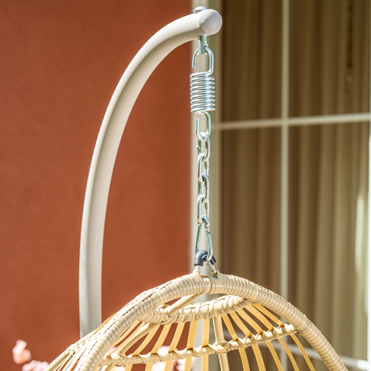 Een hangende mandstoel van rotan hangt aan een ketting aan een standaard.
