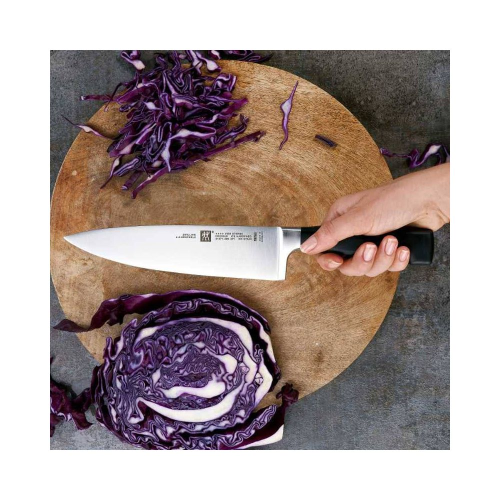 Dłoń trzyma nóż kuchenny nad czerwoną kapustą na drewnianej desce.