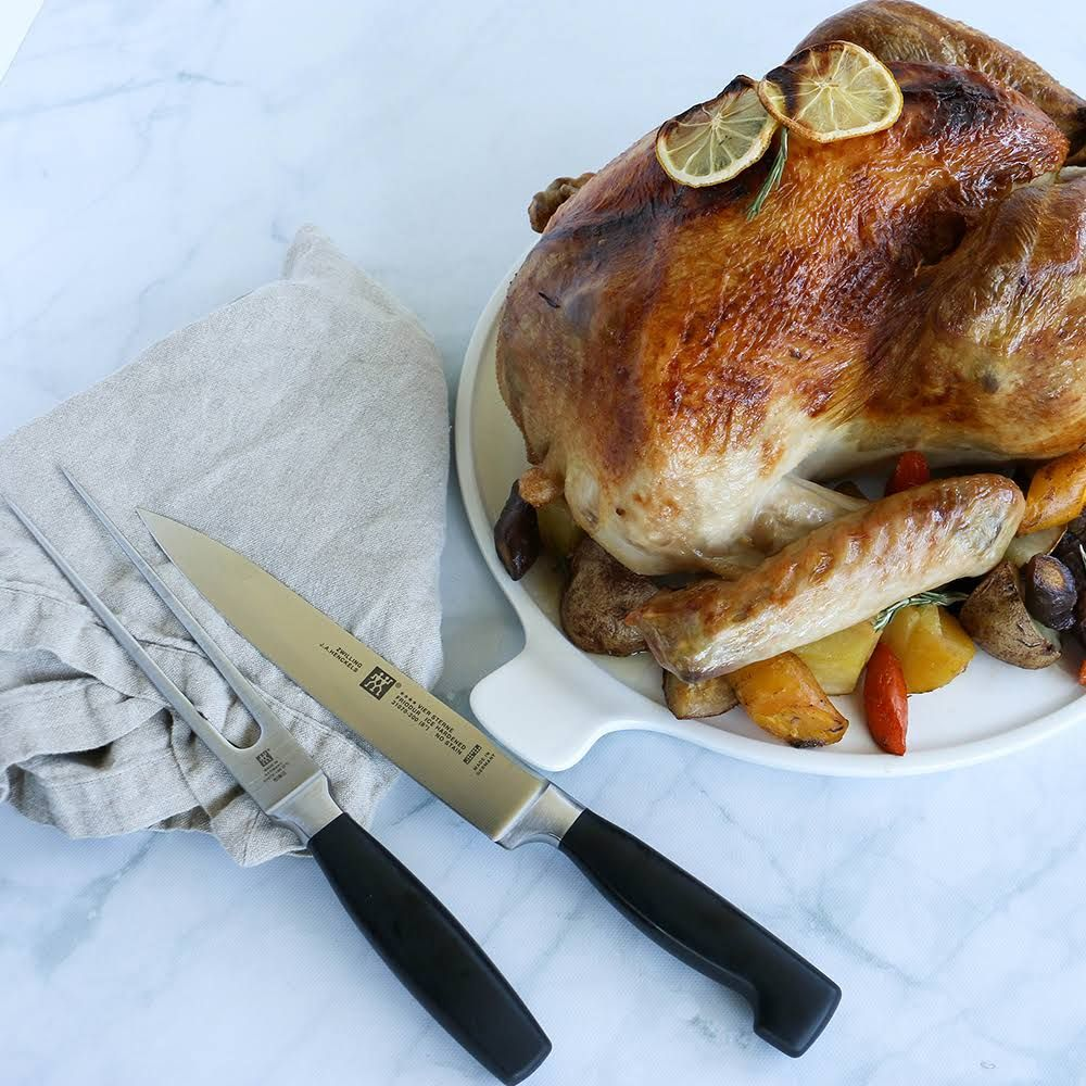 Pieczony indyk z warzywami na białej tacy, obok nóż i widelec.