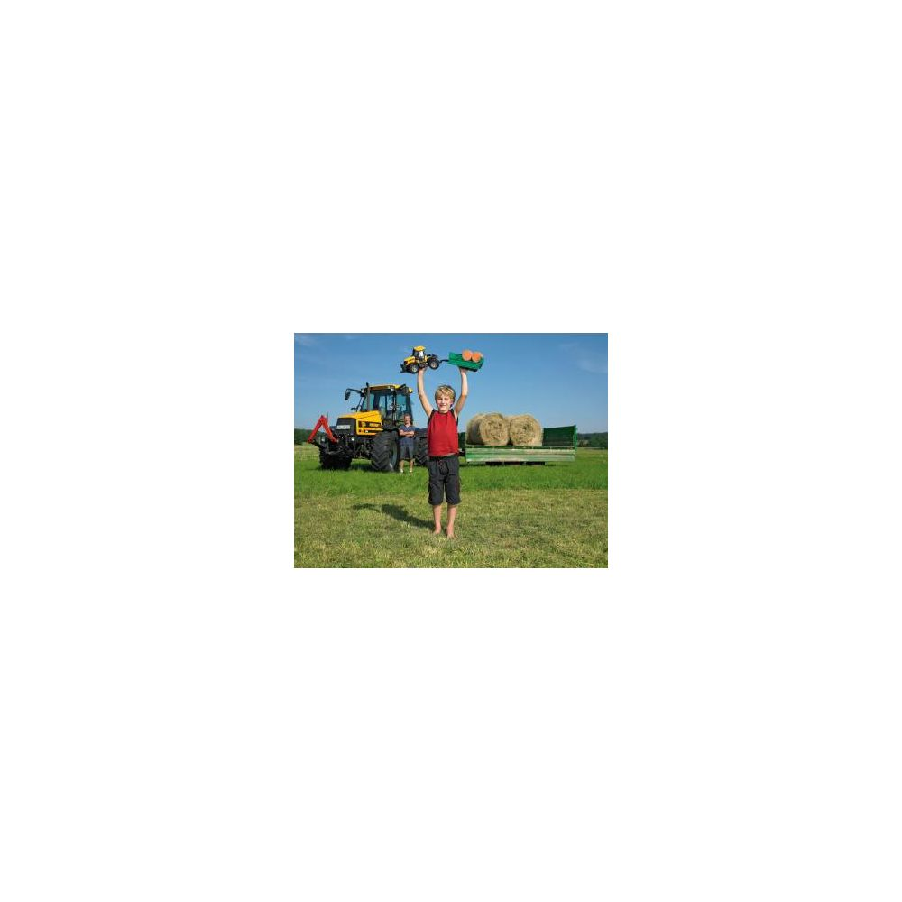 Junge hält Spielzeugtraktor über Kopf, Traktor und Ballen im Hintergrund.