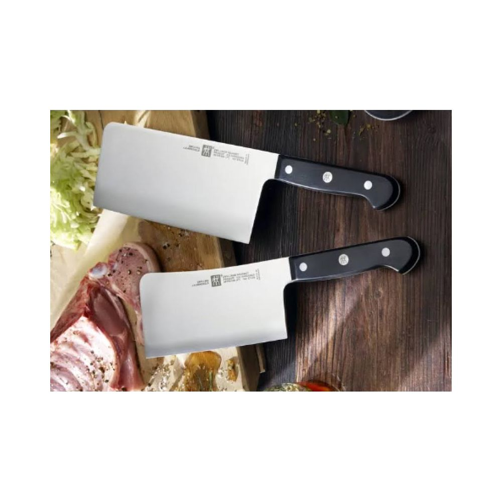 Dwa tasaki z czarnymi rękojeściami leżą obok surowego mięsa i kapusty.