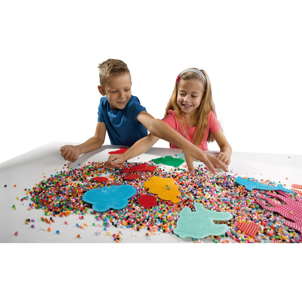 Dos niños hacen manualidades con cuentas y formas de colores en una mesa.