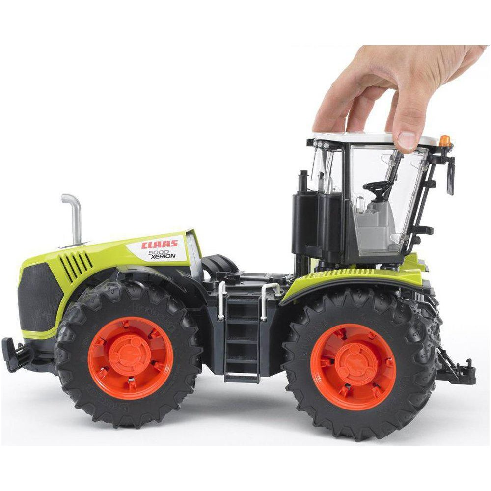 Ręka trzyma dach zielonego traktora-zabawki z pomarańczowymi felgami.