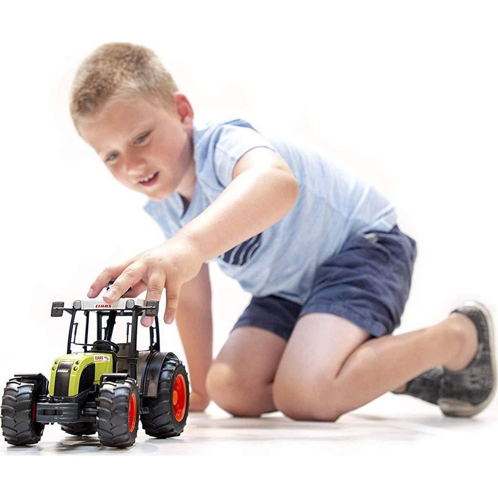 Chłopiec klęczy i bawi się zabawką traktora.