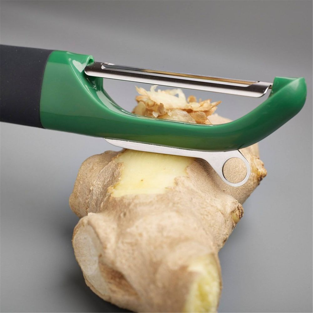 A green peeler is peeling ginger on a gray background.