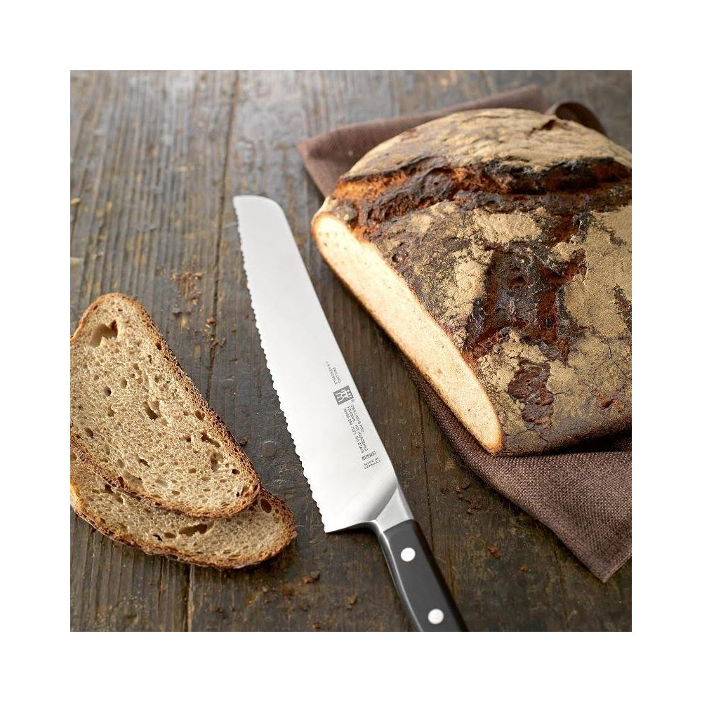 Nóż do chleba obok bochenka i dwóch kromek na drewnianym stole.