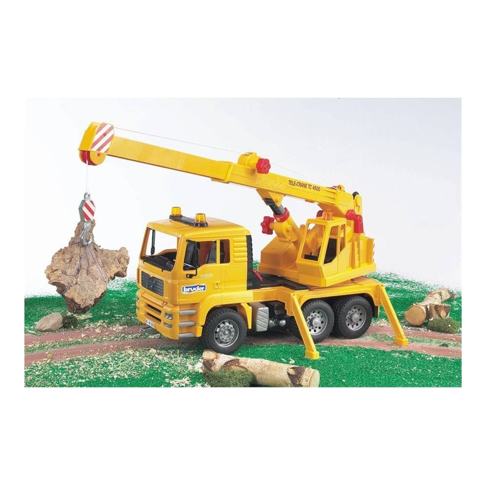 Żółty dźwig zabawkowy podnosi kloc w zielonym krajobrazie.