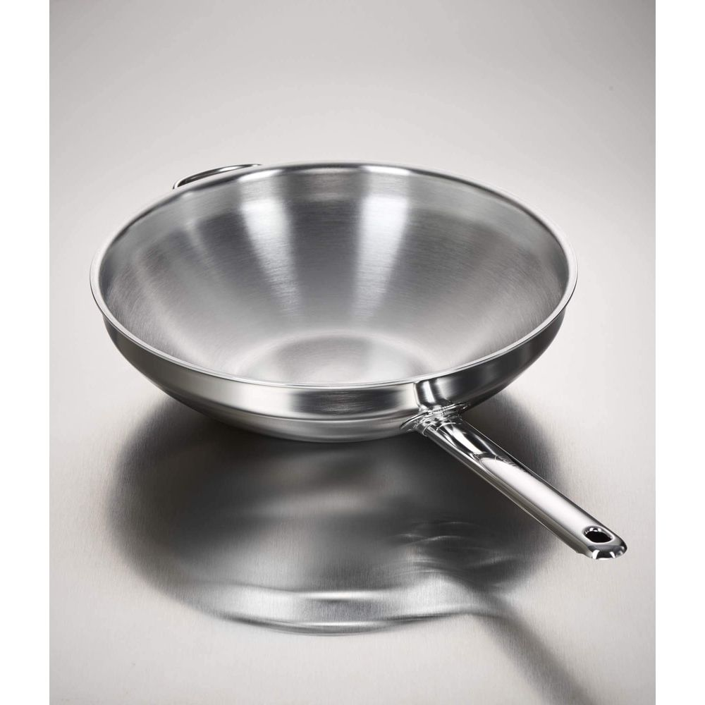Eine glänzende Edelstahl-Wokpfanne mit Griff auf einer Metalloberfläche.