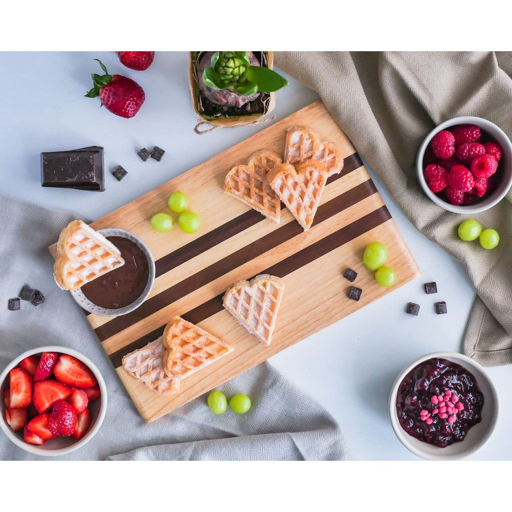 Herzförmige Waffeln mit Beeren, Trauben und Schokoladenstückchen auf einem Holzbrett.