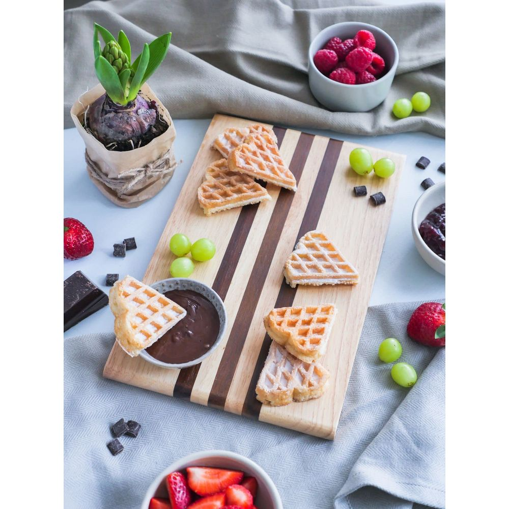 Waffeln mit Schokoladendip, Himbeeren, Erdbeeren und Trauben auf einem Holzbrett.