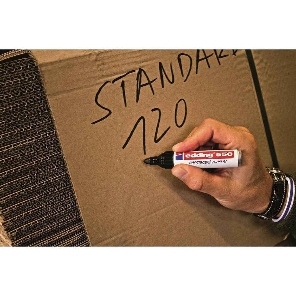 Hand schreibt Standard 120 mit Edding-Marker auf Karton. Links Stapel.