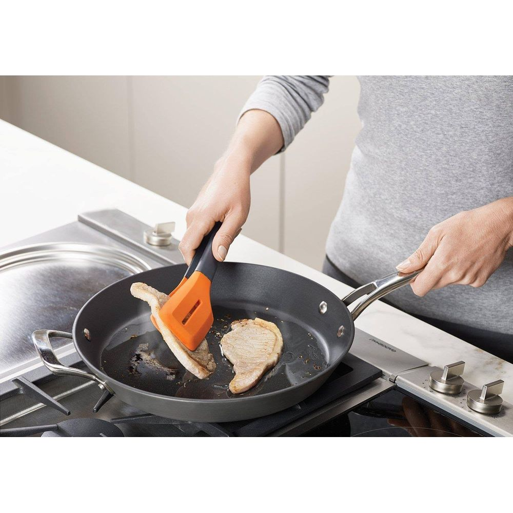 Una persona fríe carne en una sartén con un utensilio de cocina naranja.