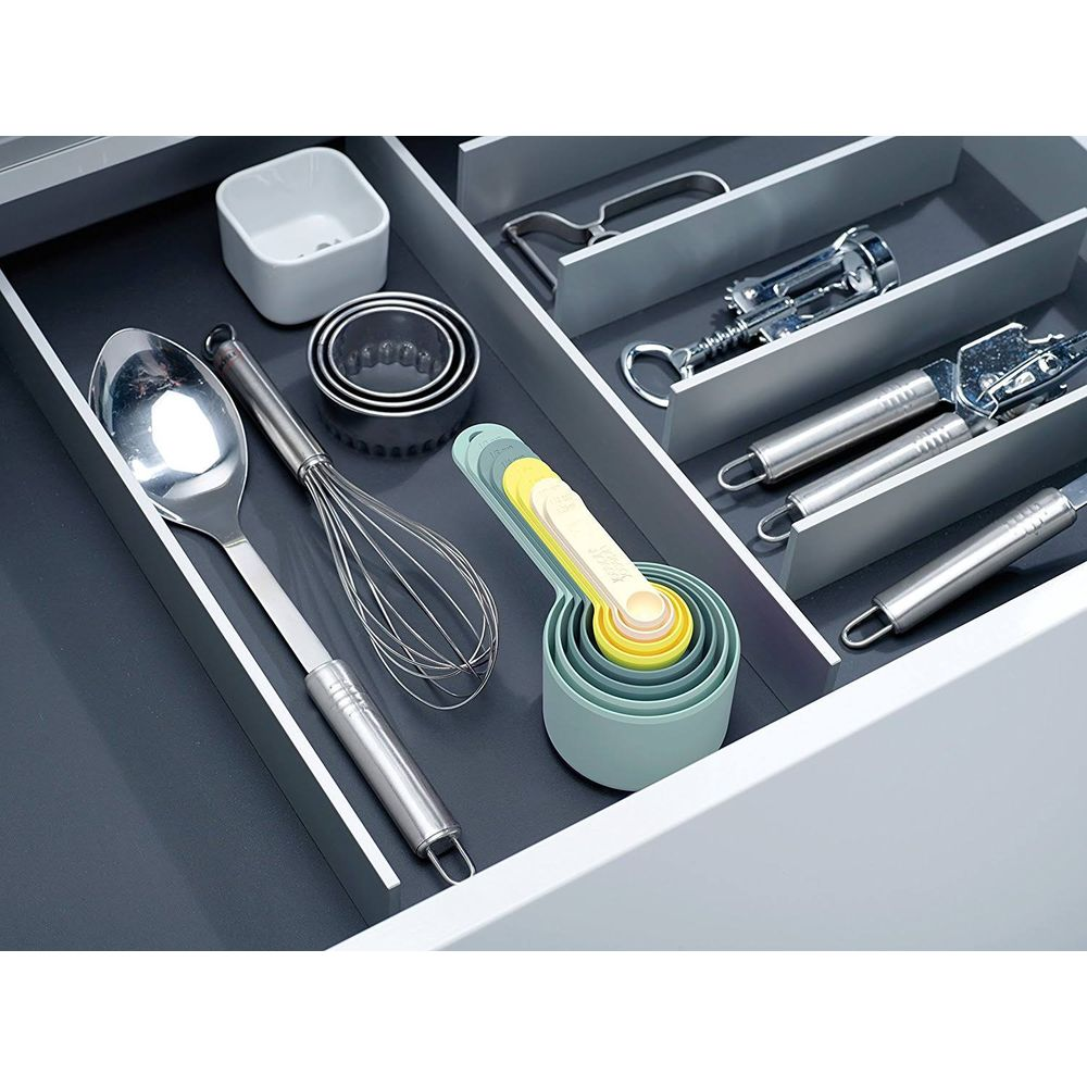 Un cassetto da cucina contiene utensili: cucchiaio, frusta, formine per biscotti, misurini e pelapatate.
