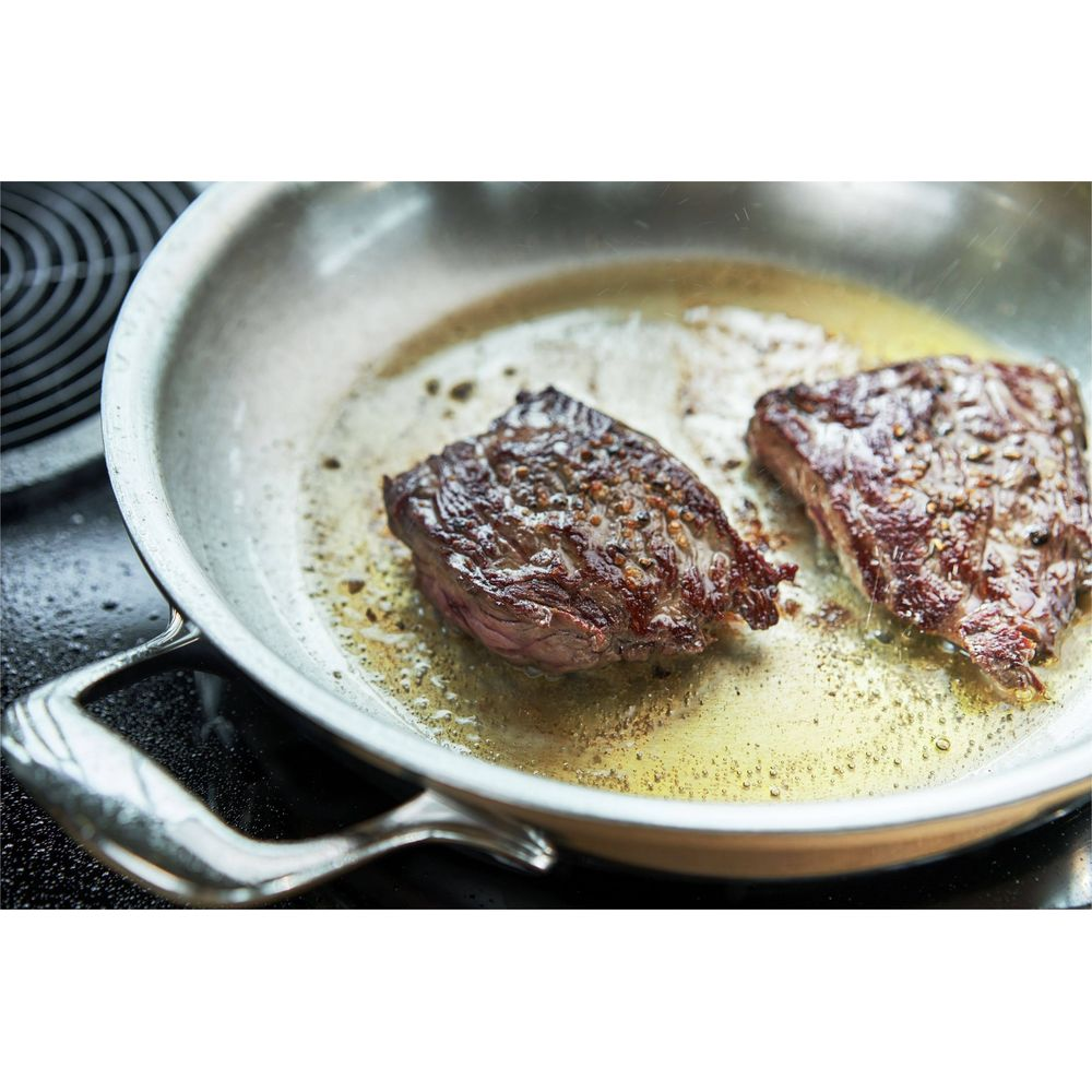 Deux steaks grésillant dans une poêle avec de l'huile et des épices.