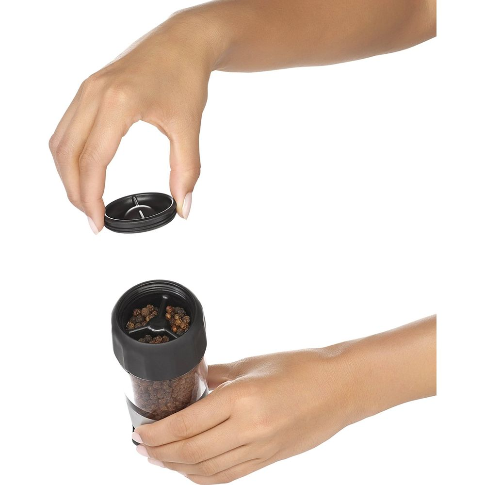 Dłonie otwierają młynek do pieprzu z ziarnami pieprzu.