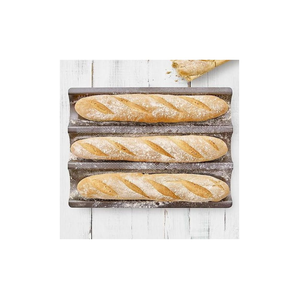 Drei Baguettes auf einem Backblech, mit Mehl bestäubt, auf einem Holztisch.