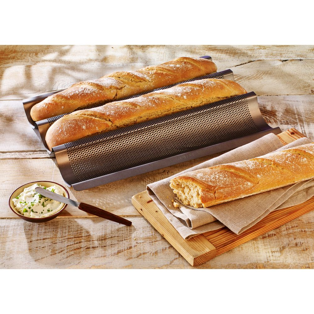 Drei Baguettes in einer Backform, eines daneben auf einem Holzbrett mit Butter.