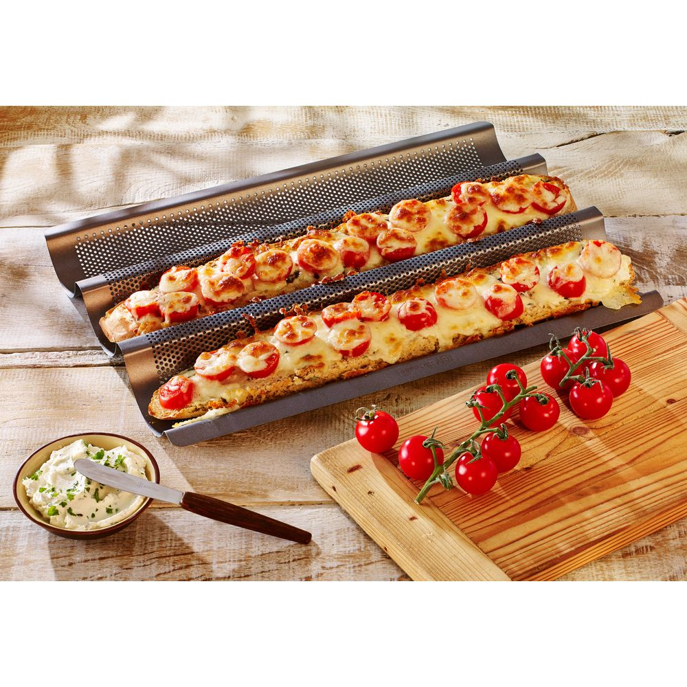 Zwei gebackene Baguettes mit Tomaten und Käse in einem Backblech auf Holztisch.
