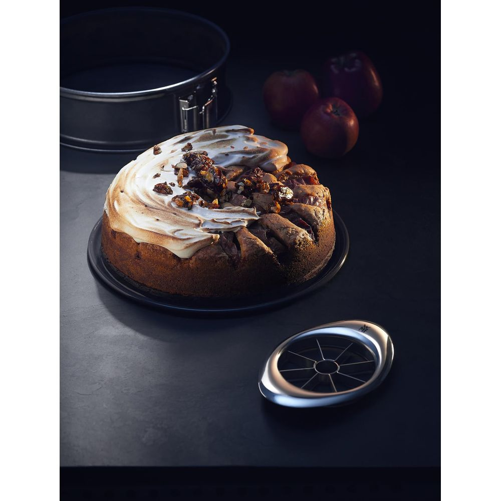 Apfelkuchen mit Baiser und Nüssen, daneben ein Apfelschneider, Backform und Äpfel.