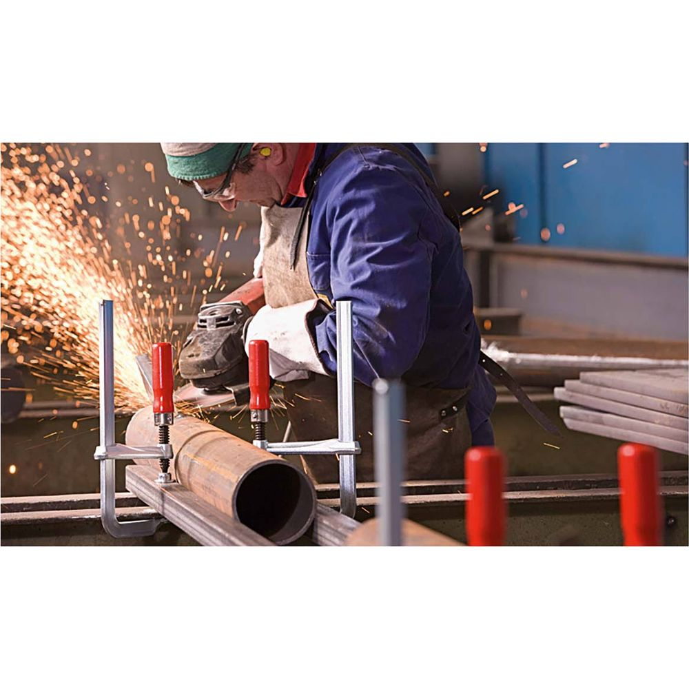 Ein Arbeiter schleift ein Metallrohr, Funken sprühen. Werkzeuge sind sichtbar.