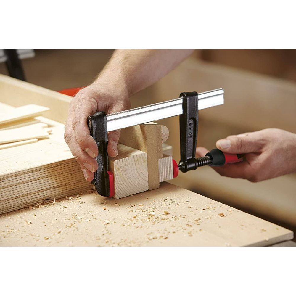 Hände halten Holzstücke mit einer Zwinge auf einer Werkbank zusammen.