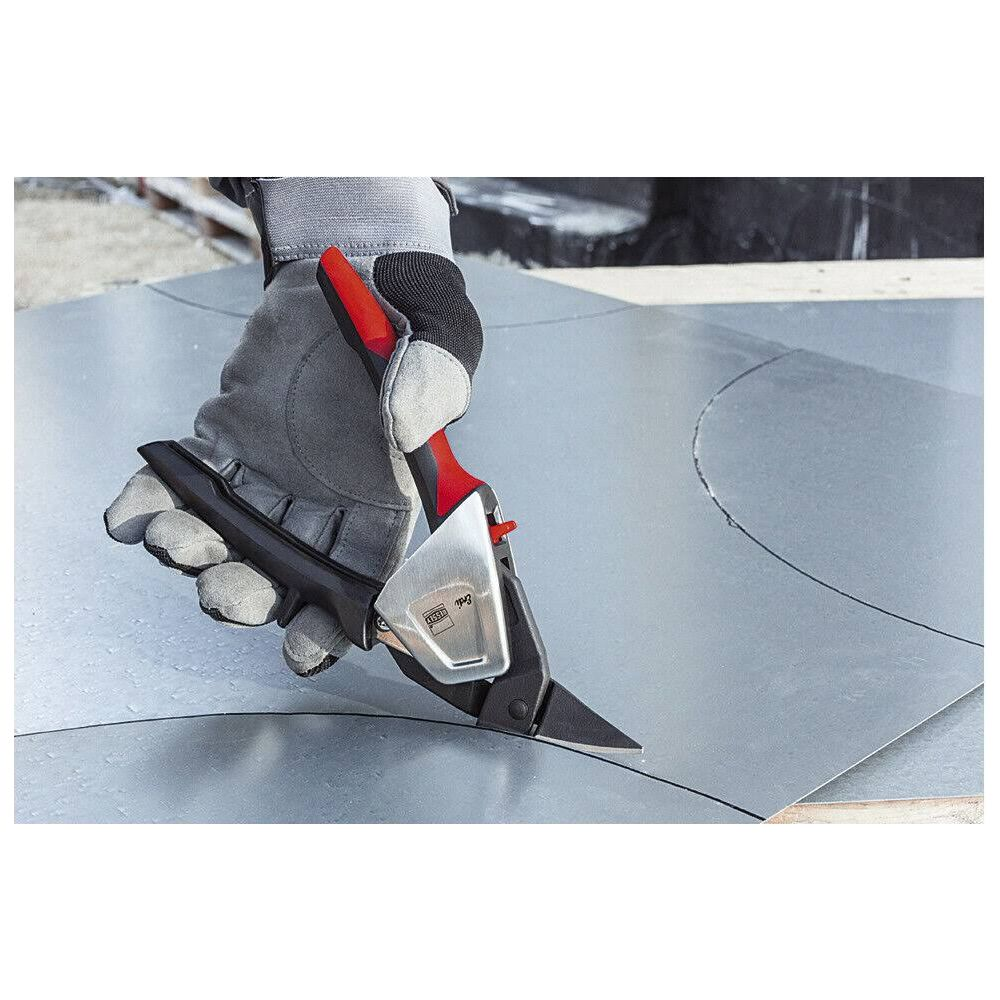 Hand mit Handschuh schneidet mit Schere Metallblech auf einer Holzoberfläche.