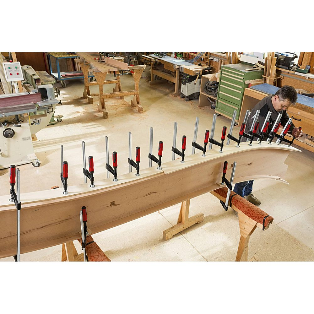 Ein Mann klemmt Holz in einer Werkstatt an eine geschwungene Form.