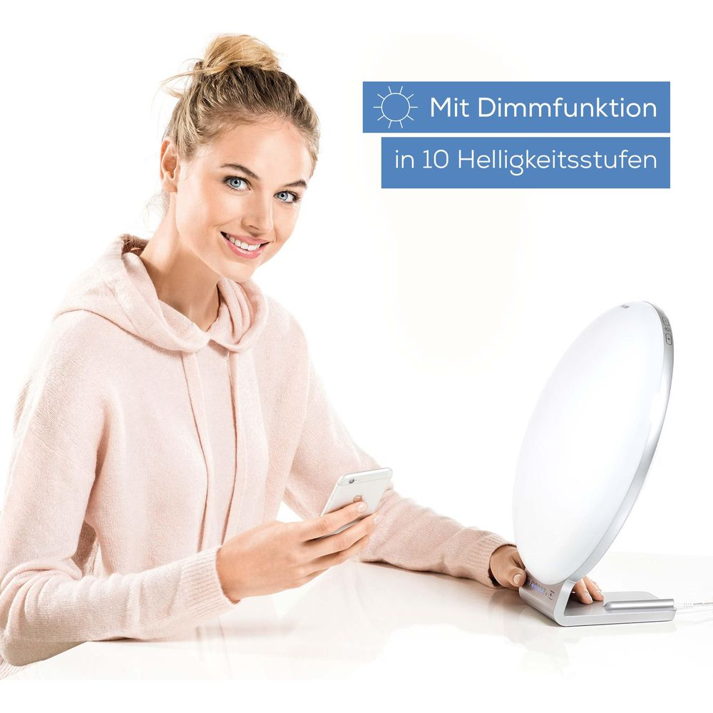 Woman with phone near light therapy lamp with 10 brightness levels.