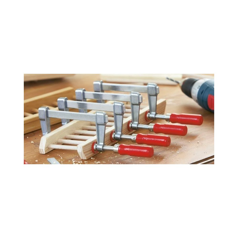Cztery drewniane ściski z czerwonymi uchwytami chwytają drewno.