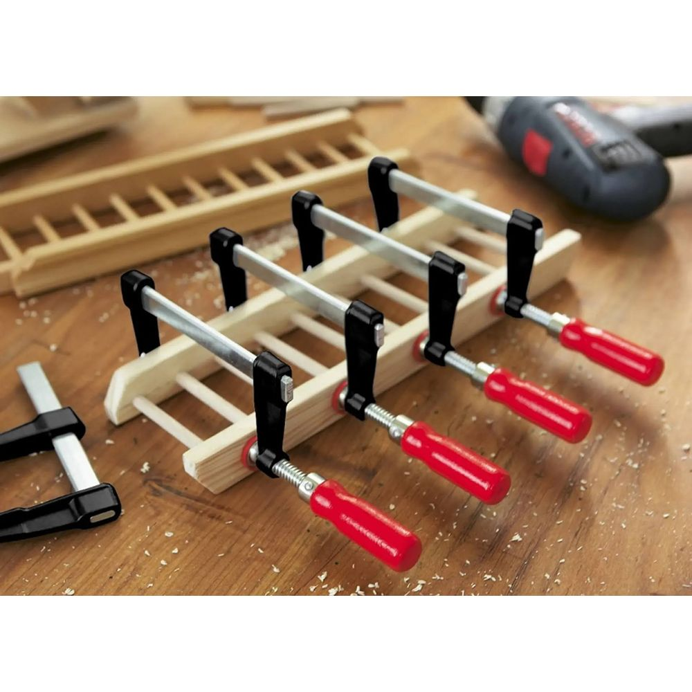 Drewniany przedmiot z czterema ściskami z czerwonymi rączkami na drewnianym stole.