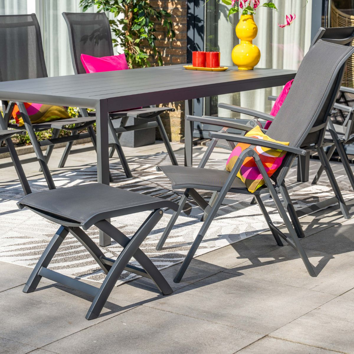 Een grijze tuintafel en stoelen met kleurrijke kussens op een terras.