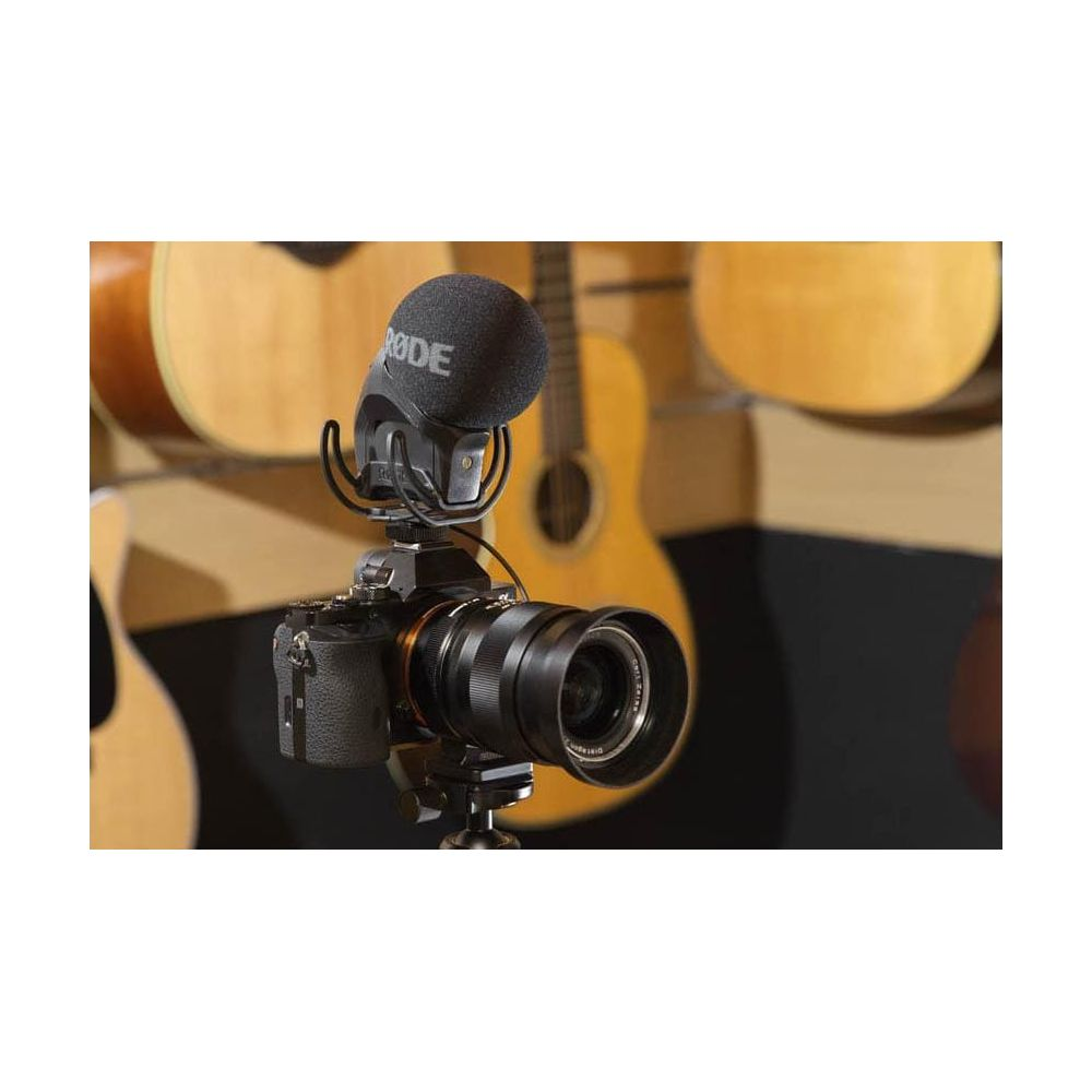 Eine Kamera mit Mikrofon steht im Vordergrund, im Hintergrund sind Gitarren zu sehen.