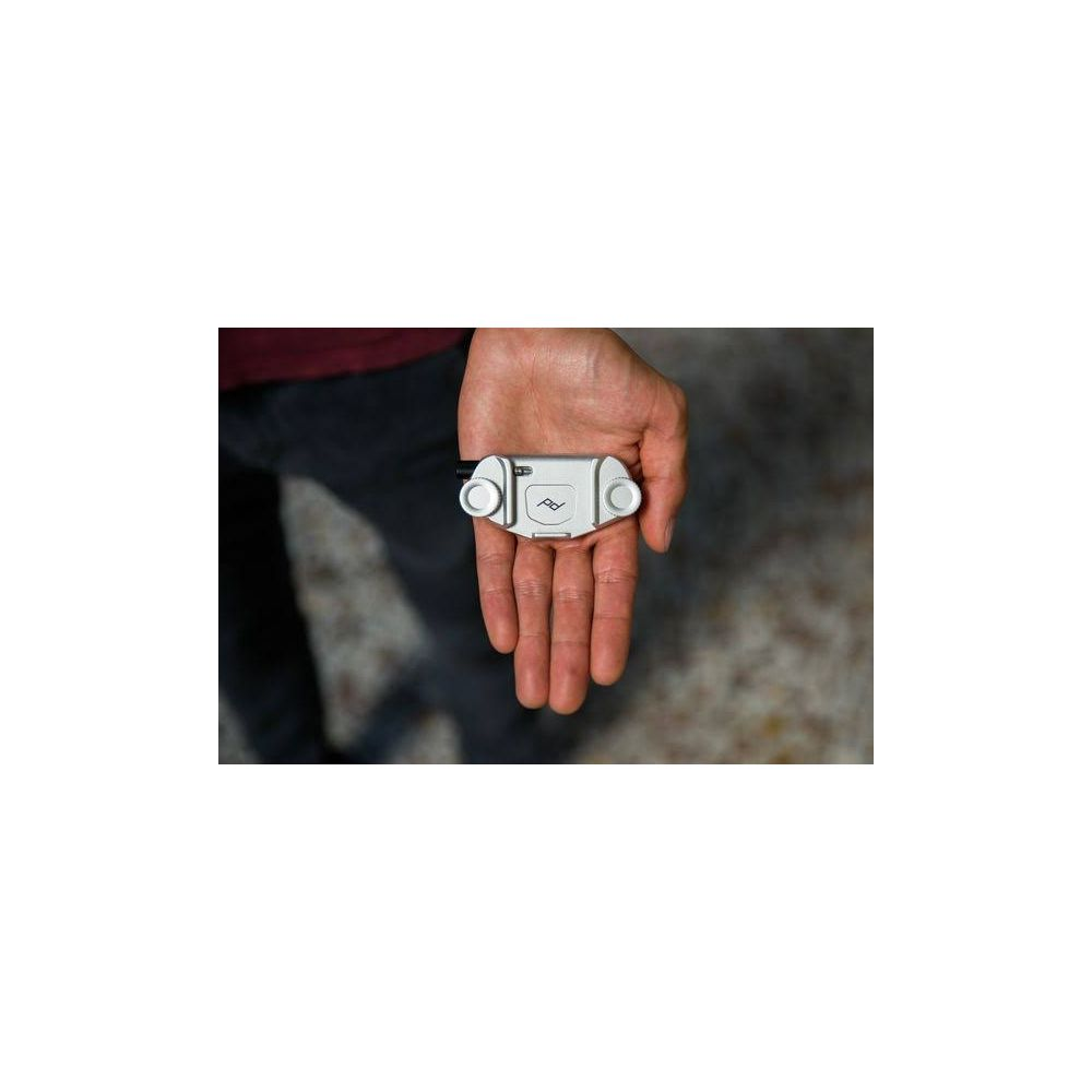 Dłoń trzyma małe srebrne urządzenie z dwoma przyciskami i logo.