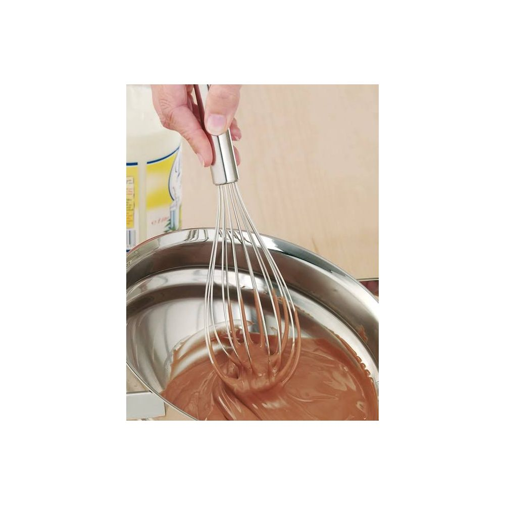 Una mano tiene una frusta che mescola pastella al cioccolato in una ciotola di acciaio inox.