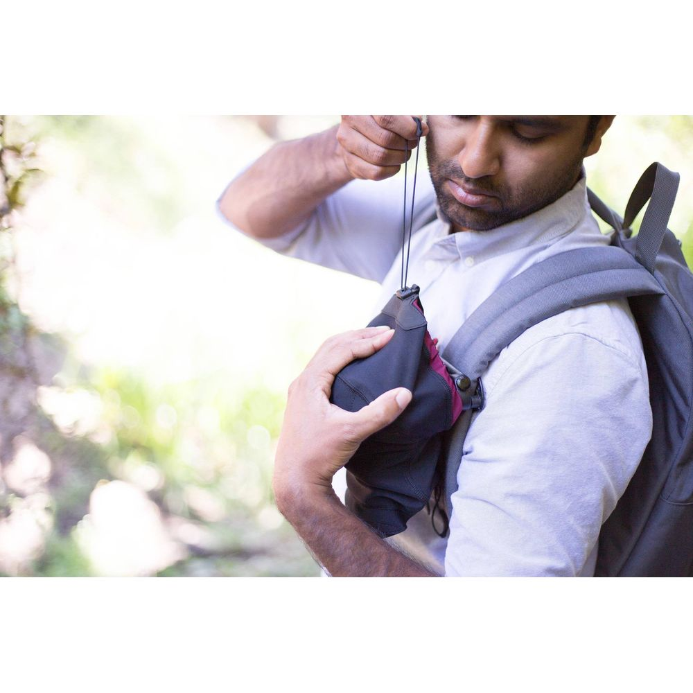 Man with backpack pulls a cord on a black bag.