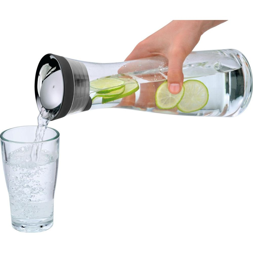 Hand gießt Wasser mit Limettenscheiben aus einer Karaffe in ein Glas.