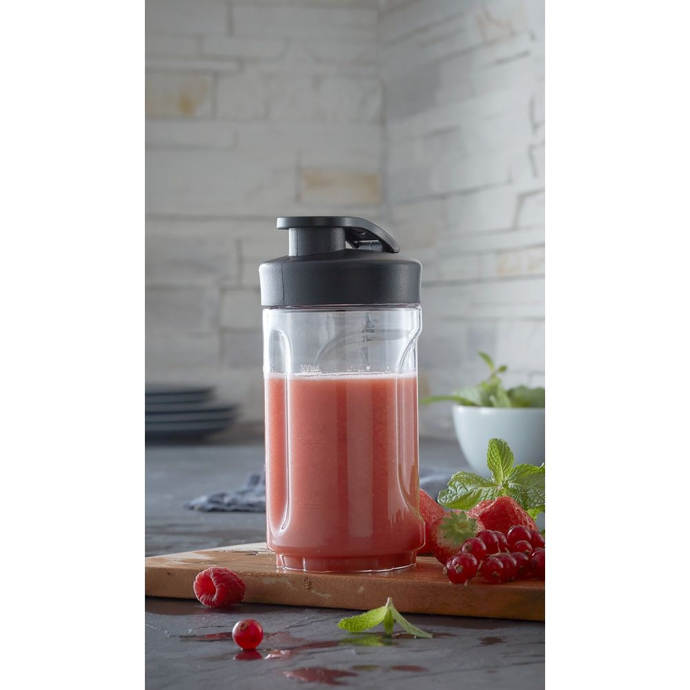 Un contenitore trasparente con frullato rosso e coperchio nero, con bacche e menta accanto.