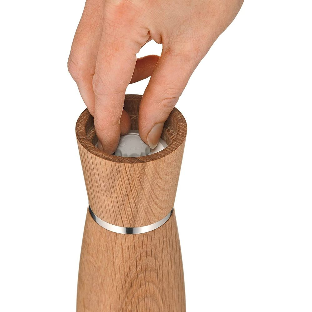 Eine Hand dreht den Einstellknopf eines hölzernen Pfeffermühlenaufsatzes.