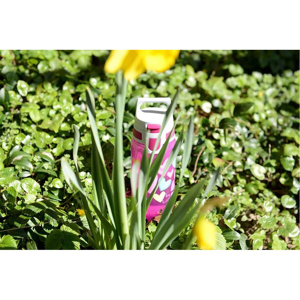 Eine pinke Wasserflasche mit Herzen liegt im grünen Gras.