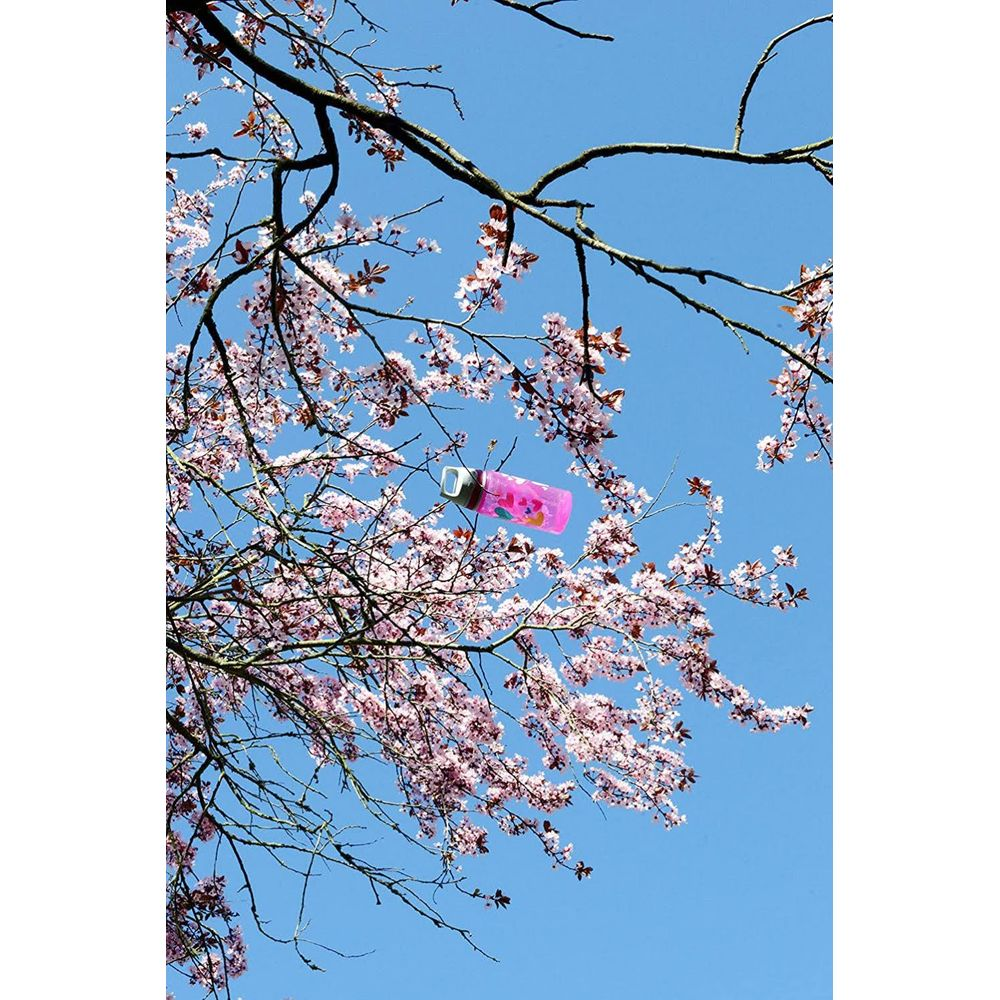 Eine rosafarbene Flasche hängt zwischen blühenden Kirschbäumen vor blauem Himmel.