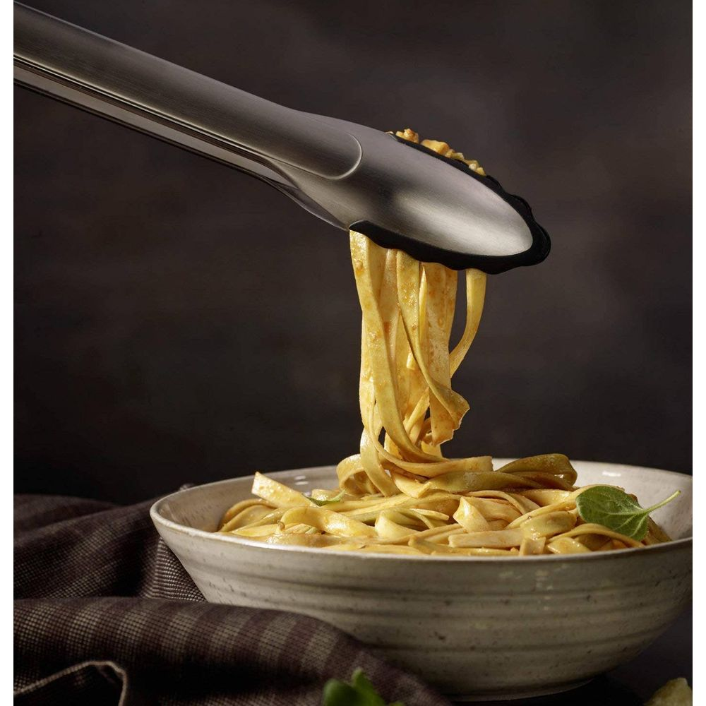 Käfig hebt Bandnudeln mit Sauce aus einer Schüssel. Dunkler Hintergrund.