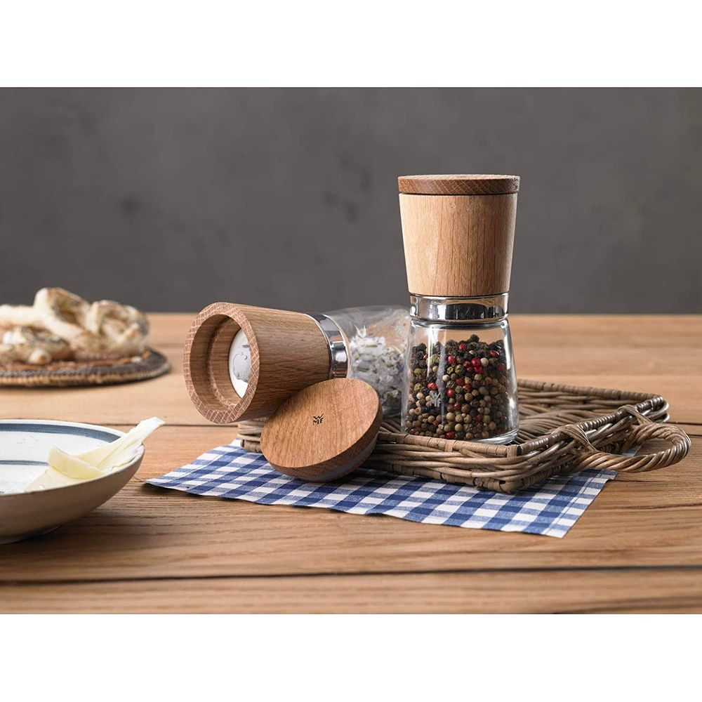 Zwei Mühlen aus Holz und Glas, gefüllt mit Pfefferkörnern, auf einem karierten Tuch.
