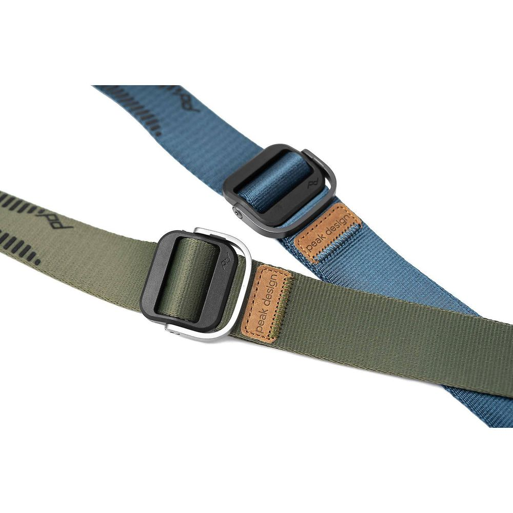 Dwa paski Peak Design, jeden oliwkowozielony, drugi niebieski, z czarnymi klamrami.