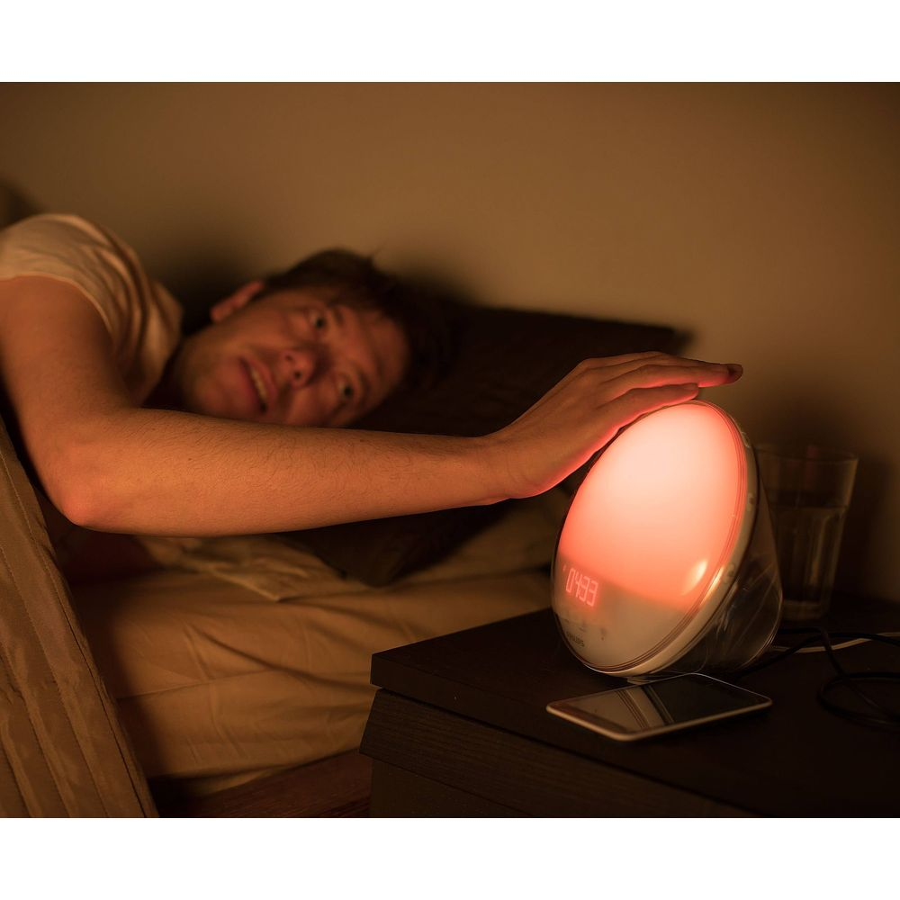 Homme au lit touche un réveil rougeoyant affichant 04:33.