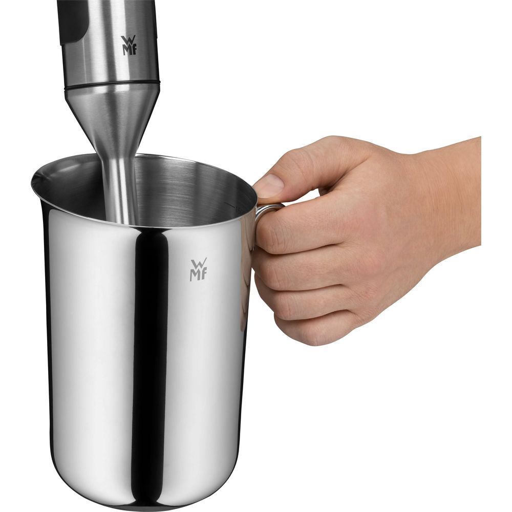 Hand hält Metallbecher, Stabmixer wird eingeführt.