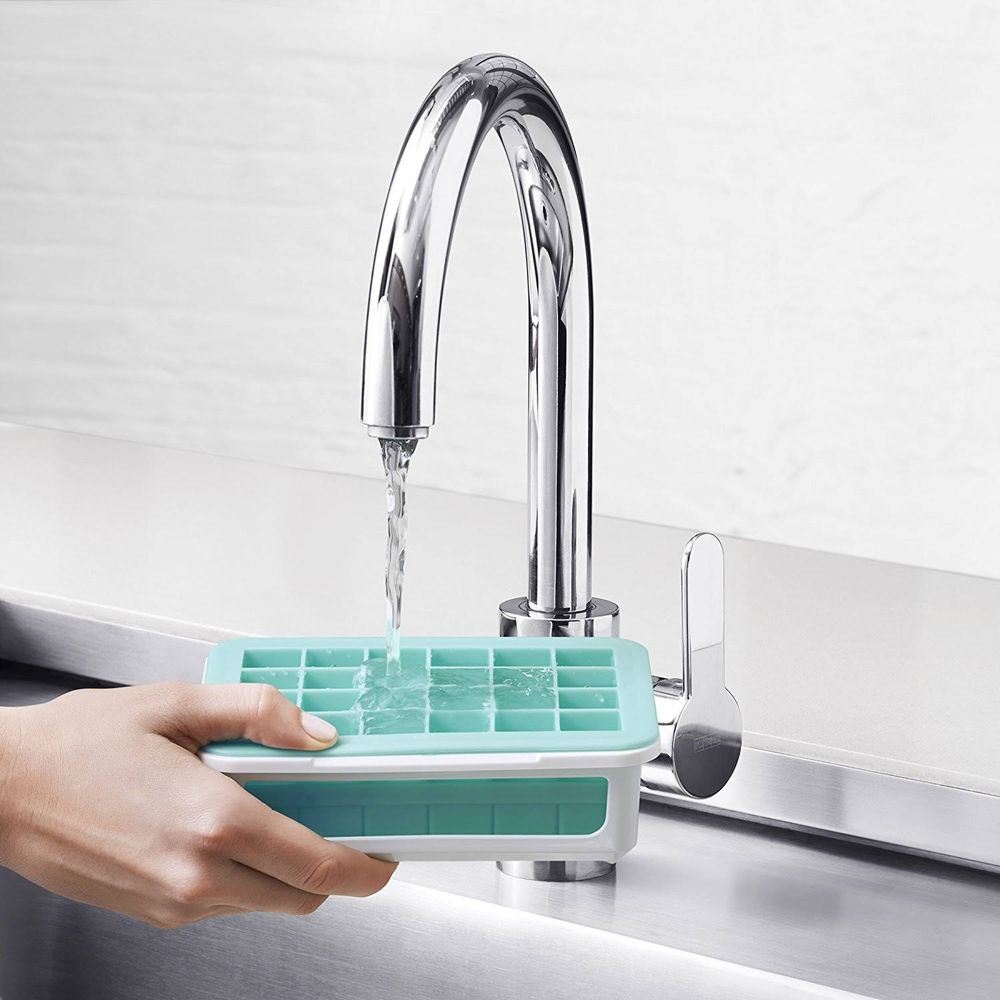 Eine Hand hält eine grüne Eiswürfelform unter fließendem Wasser aus einem Chromhahn.