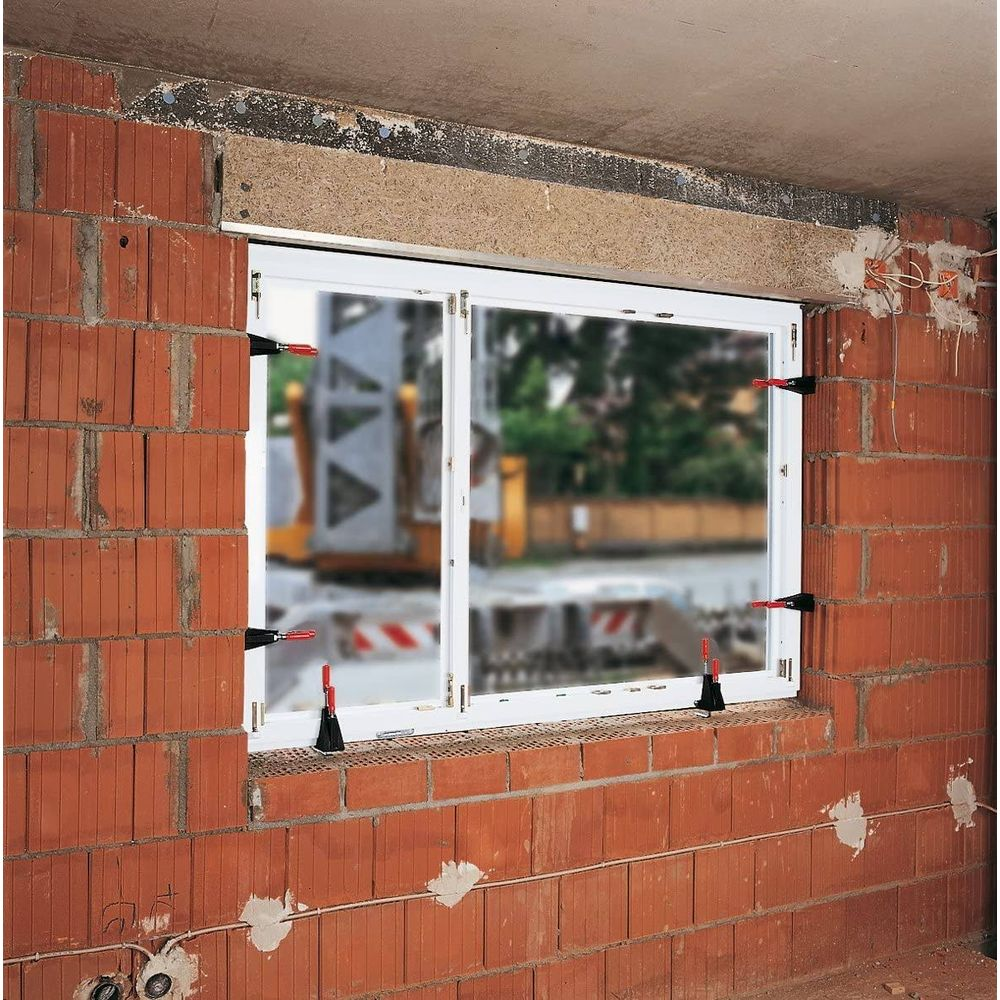Fensterrahmen wird mit roten Keilen in rotem Ziegelmauerwerk befestigt.