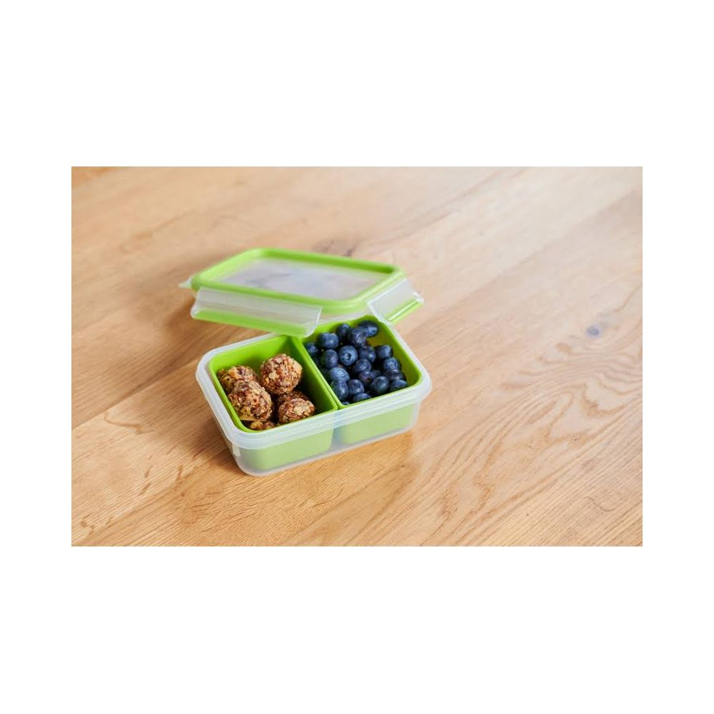Eine grüne Brotdose mit zwei Fächern auf Holztisch. Ein Fach enthält Blaubeeren, das andere Energieriegel.