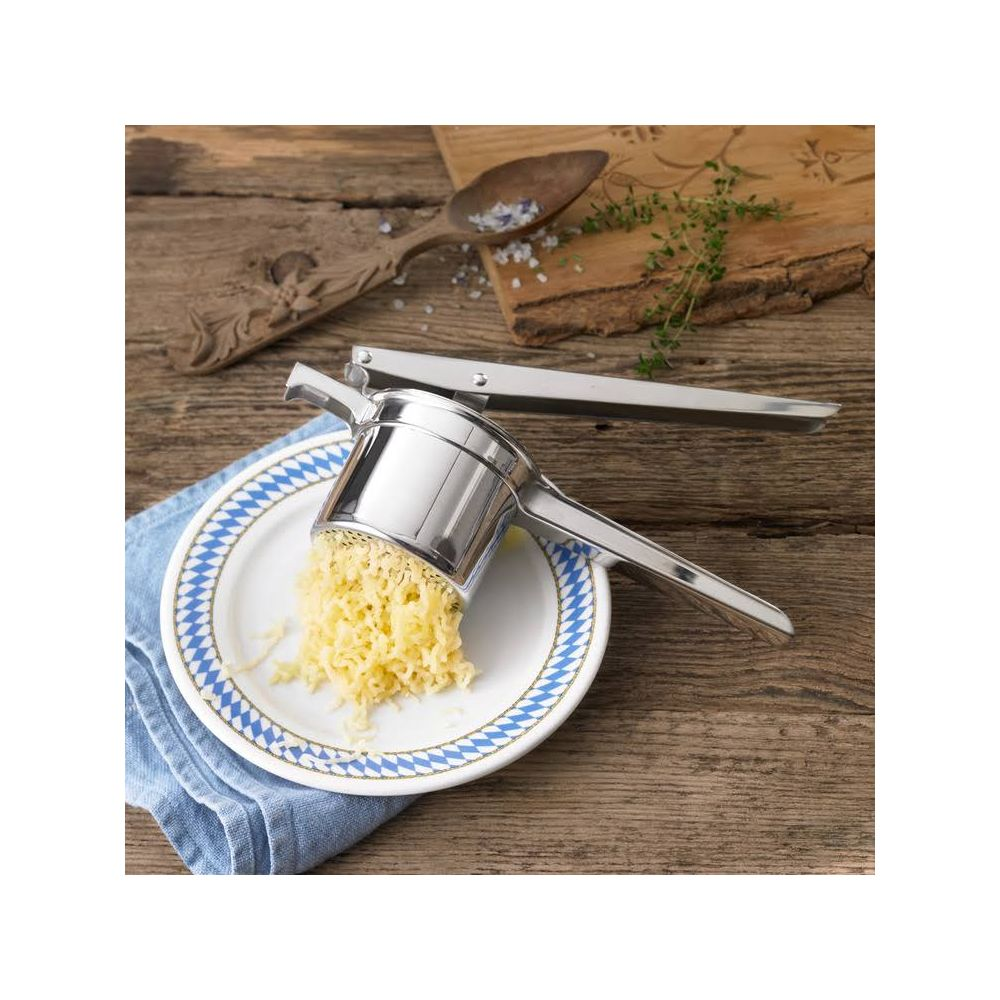 Kartoffelpresse aus Metall presst geriebene Kartoffeln auf einen Teller.