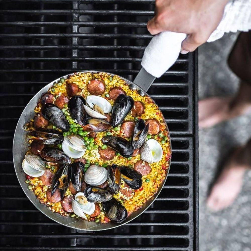 Paella auf einem Grill mit Muscheln, Wurst und Erbsen.
